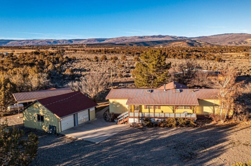 Aerial view of yellow mountain home on 10 acres in Cedaredge Colorado with detached garage and panoramic San Juan Mountain views.