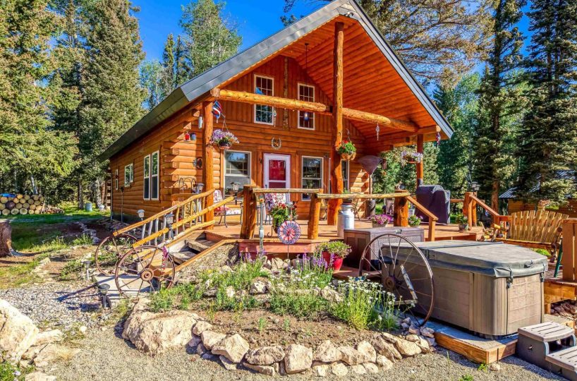 Colorado mountain cabin for sale in Cimarron: Rustic log exterior, spacious deck, hot tub, and landscaped yard surrounded by pine trees.