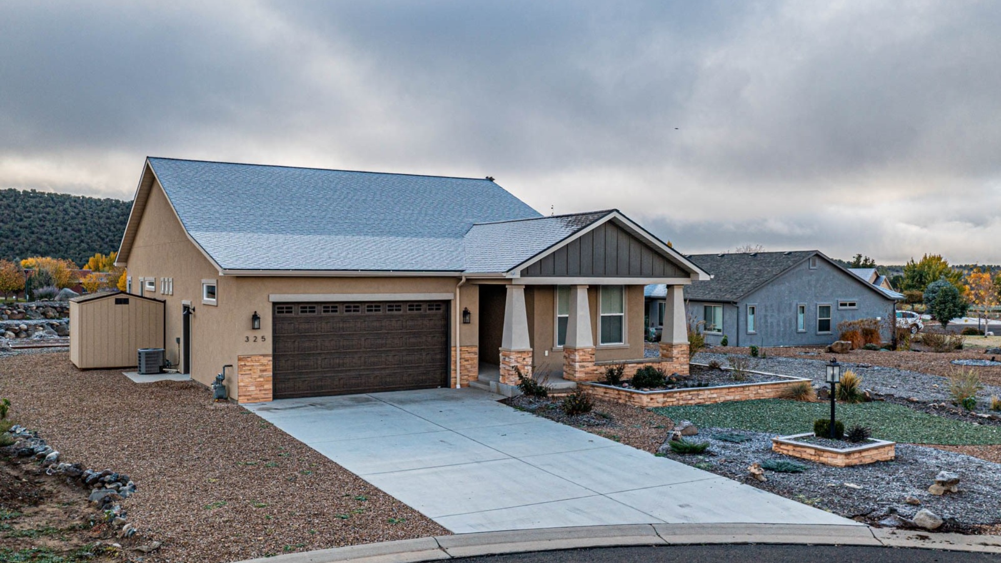 Modern single-story home with tan stucco exterior, brown garage door, and desert landscaping in Western Colorado neighborhood, showcasing affordable housing options amid rising interest rates.